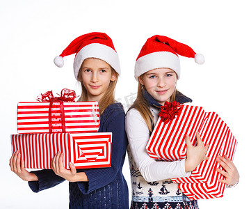 带帽子的女孩摄影照片_两个戴着圣诞老人帽子的女孩，带着礼品盒