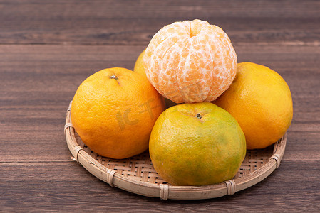 深色木桌上的竹筛上新鲜、美丽的橙色橘子。