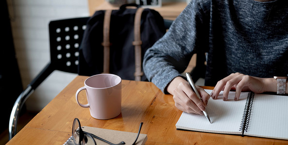在家里用笔记本电脑在记事本中工作或在线学习的女性写作制作列表记笔记的裁剪照片手