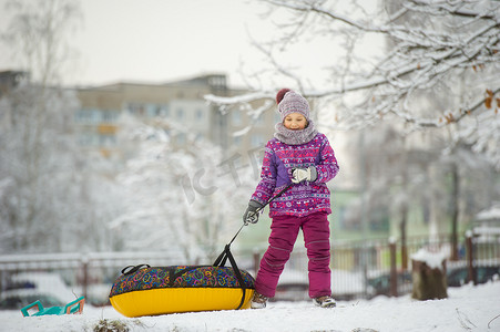 一个冬天穿着紫色衣服和充气圈的小女孩在白雪覆盖的森林里走在街上