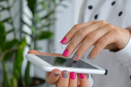 修剪整齐的女性双手，带有时尚的粉红色指甲，手持手机。