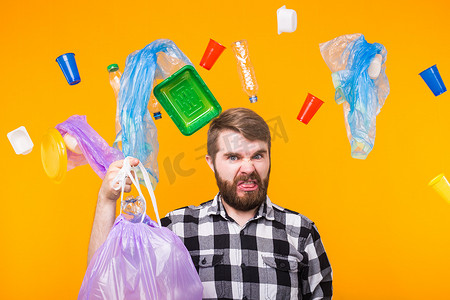 环境污染、塑料回收问题和生态问题概念-黄色背景下拿着垃圾袋的不高兴的人。