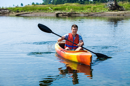 安全背心摄影照片_身穿安全背心的男子独自在平静的河面上划皮划艇