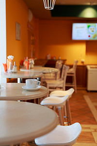 咖啡杯摄影照片_咖啡杯在咖啡厅的桌子上，背景模糊，白茶杯，早餐，咖啡厅背景橙色