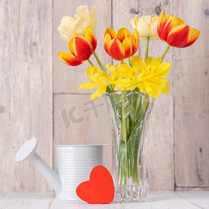 玻璃花瓶中的郁金香插花，心语问候，木桌背景墙上的喷壶装饰，特写，母亲节设计理念。