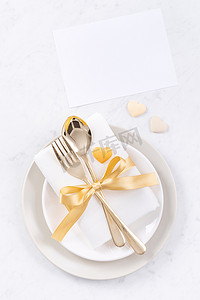 情人节、母亲节、假日约会餐、宴会设计理念-大理石背景上的白盘和金色丝带、顶视图、平躺。