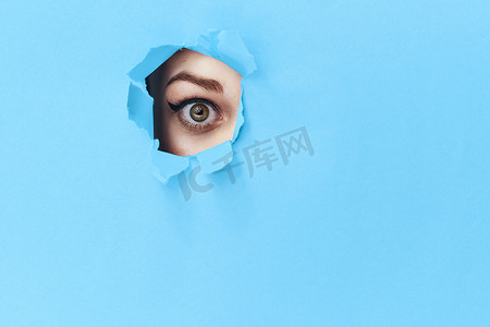 透过海报蓝色工作室背景中的孔洞窥视的女人