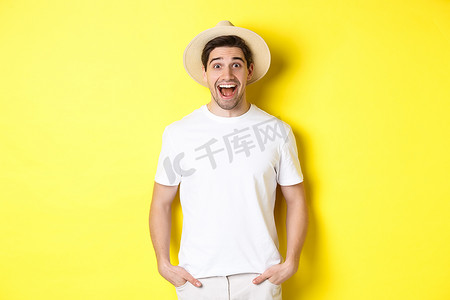 惊讶开心摄影照片_惊讶的戴草帽的男游客看起来很开心，对旅行社的广告反应惊讶，站在黄色背景上