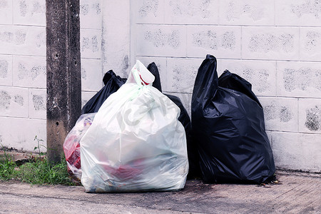 黑色垃圾塑料袋摄影照片_垃圾堆成堆，人行道社区村有许多垃圾塑料袋黑色垃圾，垃圾塑料垃圾造成的污染，塑料垃圾袋箱，垃圾堆，垃圾堆