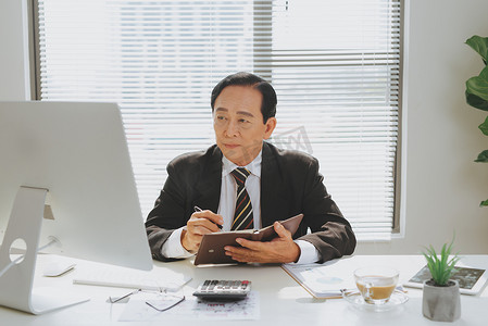 高级金融亚洲商人坐在电脑前的工作站前。