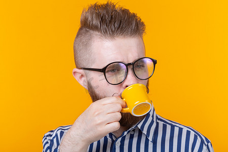可爱自信的年轻人站在黄色背景下，喝着黄色小杯子里的咖啡。
