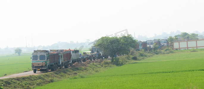 重型货车的长队交通车辆在乡村公路未铺砌的道路上排队等候。