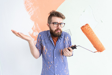 粉刷滚筒摄影照片_困惑的男性用油漆滚筒粉刷墙壁。