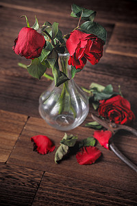 枯萎摄影照片_深灰色背景上枯萎的玫瑰和带落花瓣和落叶的木桌，悲伤情人节浪漫的设计理念，破碎，复制，空间。