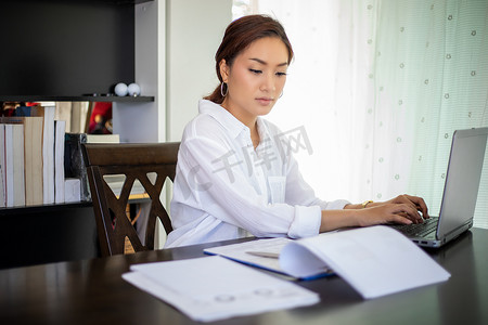 美丽的亚洲女商人检查文件并使用在家工作的笔记本来实现社交距离和自我责任概念