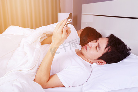 手机他摄影照片_男人在床上玩手机，而他的妻子睡在他旁边