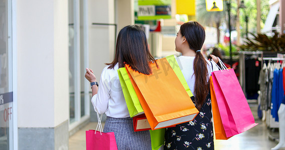 女性销售摄影照片_有朋友的亚洲女性在超市/商场购物时拿着购物袋，用智能手机微笑