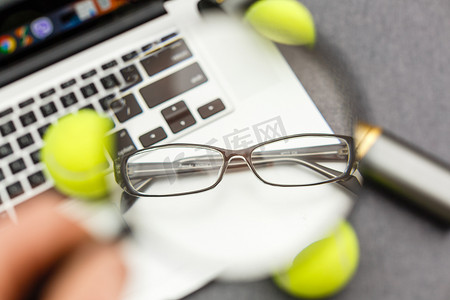 笔记本电脑、运动器材、网球、羽毛球、体育管理灰色桌子上的眼镜的顶视图。经营理念。
