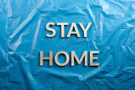 “stay home”字样在皱巴巴的蓝色塑料背景上以平躺的视角放置着银色金属字母