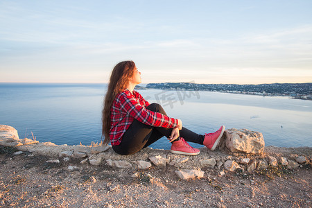 女孩望天空摄影照片_旅行、冒险和孤独的概念 — 一个女孩坐在悬崖边上望着大海