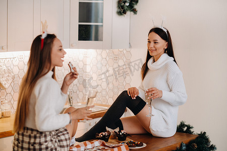 家庭环境摄影照片_两个女孩在厨房里舒适的家庭环境中，手里拿着香槟过圣诞节。