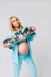 灰色背景中，一个身穿青绿色衣服、手里拿着滑板的怀孕女孩