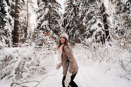 雪地里散步摄影照片_冬天，一个穿着毛衣和眼镜的女孩在白雪覆盖的森林里散步