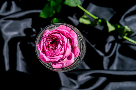 装满粉红色花瓣的酒杯放在黑色丝织品的桌子上。