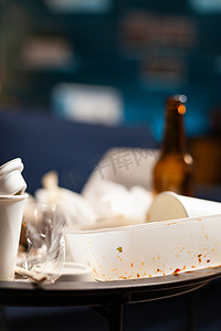 脏兮兮的空荡荡的客厅，蓝色沙发上放着食物垃圾、一瓶啤酒和餐巾纸
