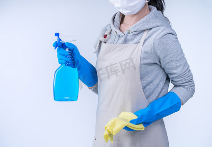 围裙的年轻女管家正在用蓝色手套、湿黄色抹布、喷瓶清洁剂、特写、复制空间、空白设计概念进行清洁。