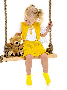 一个小女孩正抱着一只泰迪熊荡秋千。