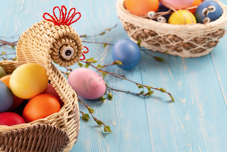 物语摄影照片_蓝木桌上放着彩色复活节彩蛋的鸡形柳条篮 — 带复制空间的复活节组合物