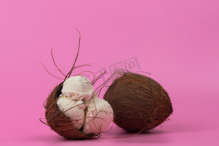 白色冰淇淋球摄影照片_粉红色背景中用薄荷叶装饰的空椰子中的香草冰淇淋球