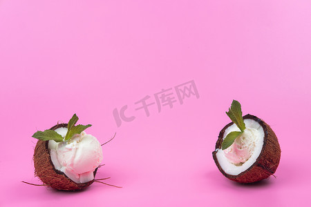 白色冰淇淋球摄影照片_粉红色背景中用薄荷叶装饰的新鲜椰子半香草冰淇淋球
