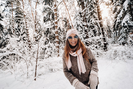 冬天，一个穿着毛衣和眼镜的女孩在白雪覆盖的森林里散步