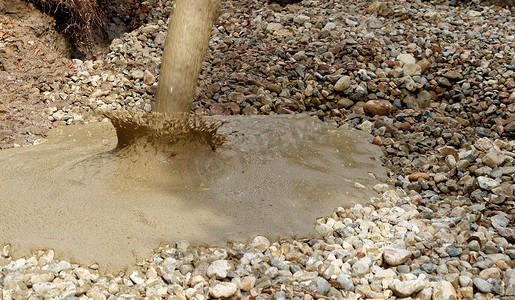 液态土壤从混凝土搅拌机中倒入铺有粗砂砾和石块的挖掘坑地面。