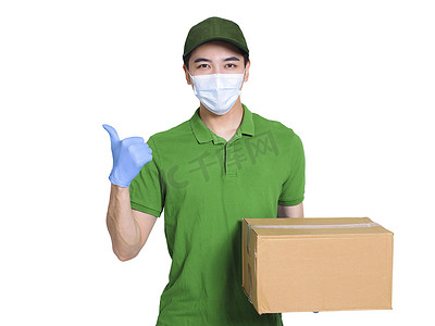年轻的快递员，穿着绿色的衣服和帽子、防护面具和手套来保护自己，在 covid-19 流行病期间运送包裹，并竖起大拇指