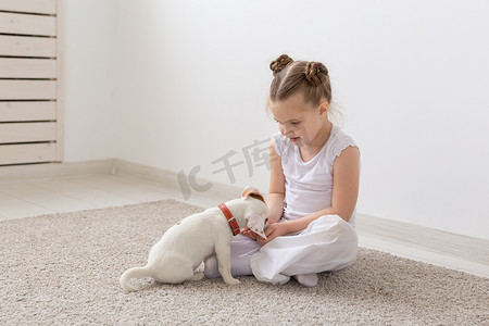 沙发上的狗狗摄影照片_儿童、宠物和动物的概念 — 穿着睡衣的小女孩在地板上和杰克罗素梗犬玩耍