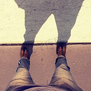 男人长腿站在街道上，有阴影的混凝土墙