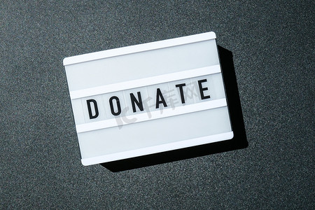 黑色背景上的灯箱板，上面写着黑色字母的捐赠字样。