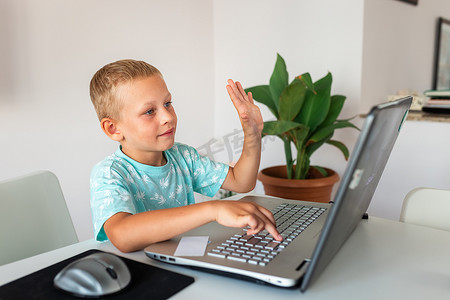 在家里用笔记本电脑和课堂笔记在虚拟课堂上学习的小男孩。