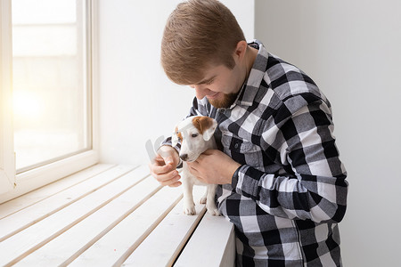 人、宠物和动物的概念 — 年轻人在白色背景的窗户附近拥抱杰克罗素梗犬