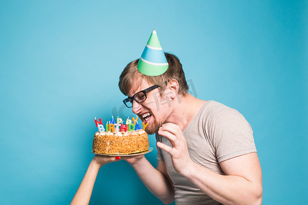 戴着问候纸帽的滑稽疯狂年轻人想咬掉一块祝贺蛋糕。