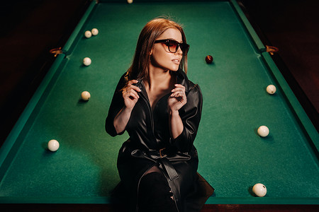 一个戴眼镜的女孩坐在俱乐部的台球桌上。俄罗斯台球
