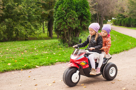 绿色公园里骑着儿童摩托车的可爱小女孩