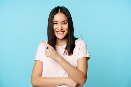 笑得开心的亚洲女模特肖像，指着左上角，展示销售横幅、商店广告、蓝色背景