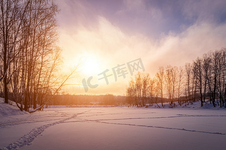 冬天，沿岸有桦树的结冰池塘上的日落或日出。