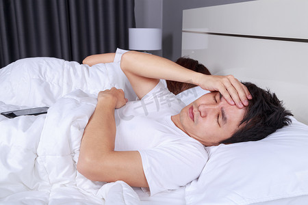 男人在床上失眠，在卧室里有偏头痛、压力、失眠、宿醉