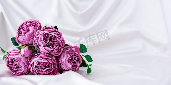 紫粉背景摄影照片_白色丝绸织物背景上美丽的紫牡丹花束。