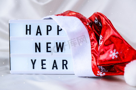 灯箱与文本新年快乐与圣诞老人帽子在丝绸织物背景。